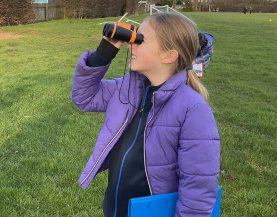 Y5 pupil bird watching on the school field.